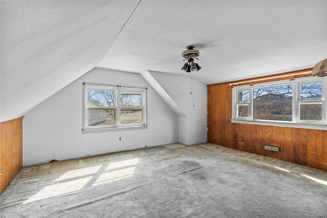 bonus room featuring vaulted ceiling, wooden walls, carpet, and a wealth of natural light