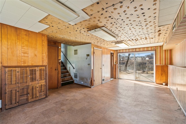 unfurnished room featuring tile patterned floors, wooden walls, and stairs