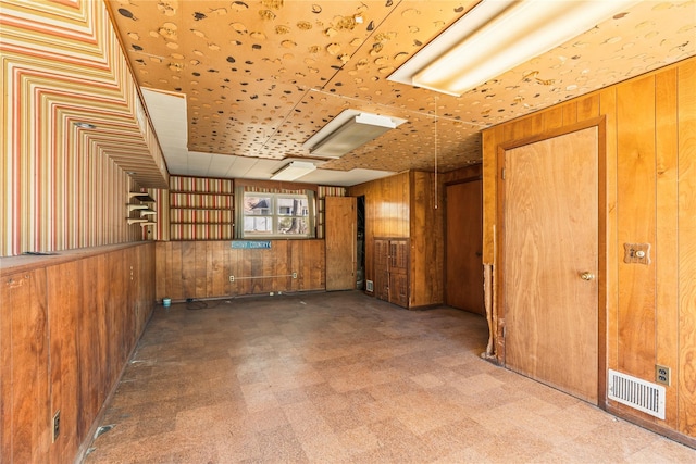 unfurnished room featuring tile patterned floors, wooden walls, and visible vents