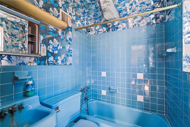 bathroom featuring wallpapered walls, a sink, shower / bath combination, tile walls, and toilet