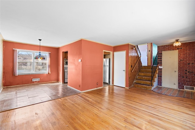 unfurnished living room featuring visible vents, baseboards, stairs, ornamental molding, and hardwood / wood-style flooring