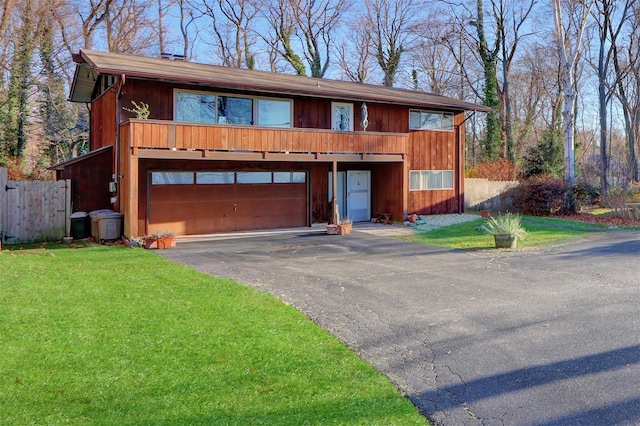 chalet / cabin featuring aphalt driveway, an attached garage, a front lawn, and fence