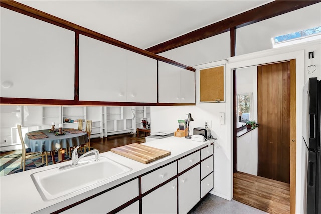 kitchen featuring beam ceiling, a sink, light countertops, white cabinetry, and refrigerator with ice dispenser