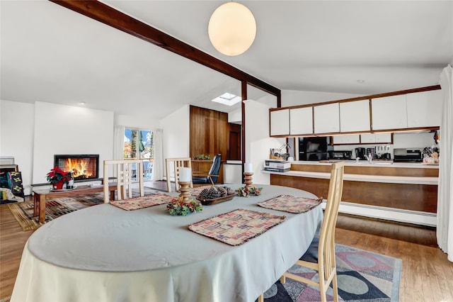 dining area with a warm lit fireplace, a baseboard heating unit, lofted ceiling with beams, and wood finished floors