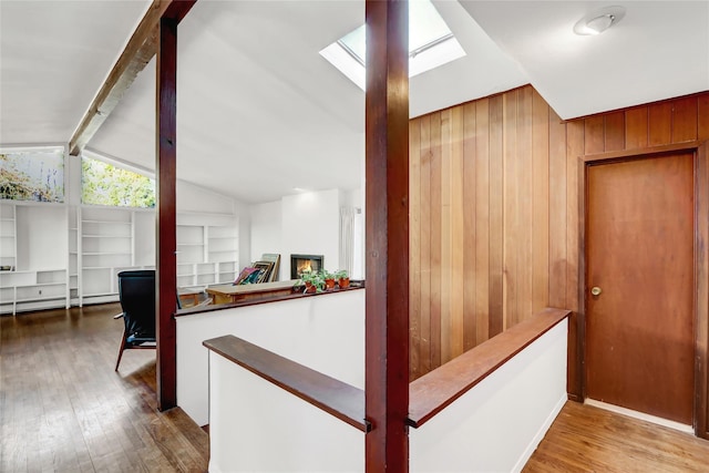 corridor featuring wooden walls, vaulted ceiling with skylight, baseboard heating, and wood finished floors