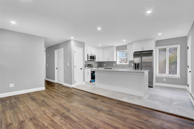 kitchen featuring a center island, light countertops, decorative backsplash, stainless steel appliances, and white cabinetry