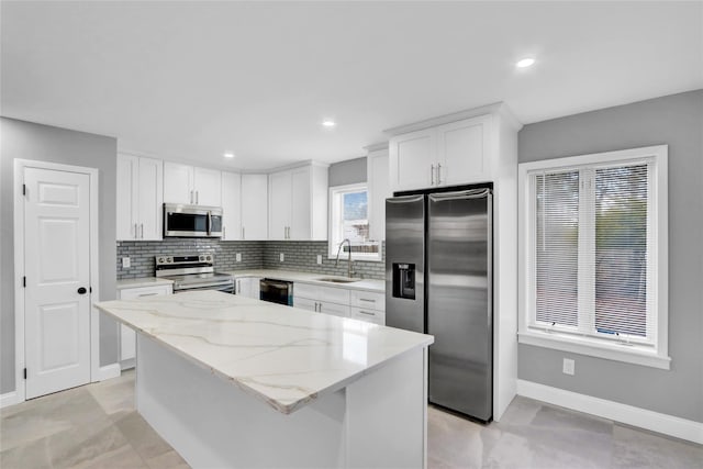 kitchen featuring light stone counters, a sink, decorative backsplash, appliances with stainless steel finishes, and a center island