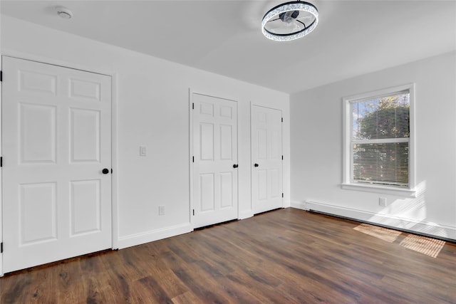 unfurnished bedroom featuring dark wood-style floors, a baseboard heating unit, and baseboards