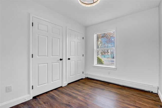 unfurnished bedroom featuring dark wood-style flooring, baseboards, and a baseboard radiator