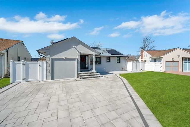 ranch-style house featuring a front yard, a gate, fence, solar panels, and stucco siding