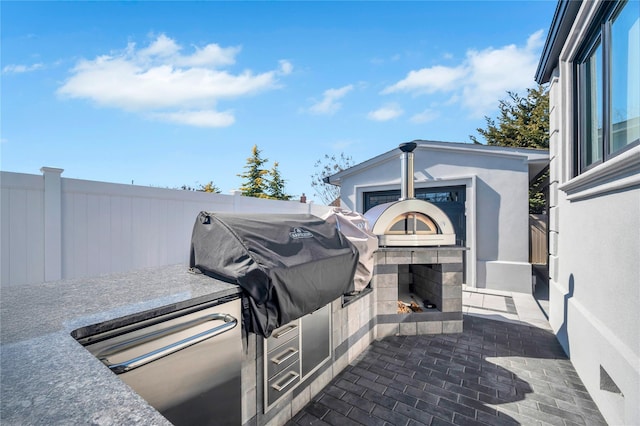 view of patio with exterior fireplace, fence, and a grill