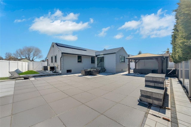 rear view of property with solar panels, a gazebo, a fenced backyard, a patio, and a gate