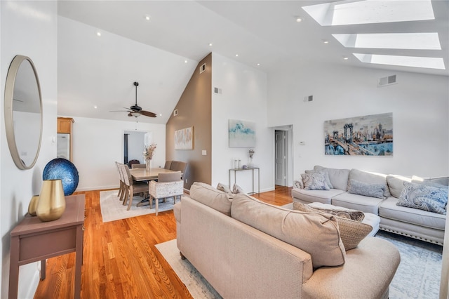 living area featuring a ceiling fan, vaulted ceiling with skylight, light wood-style floors, and visible vents