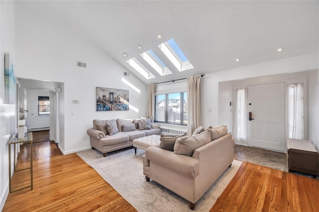 living area with visible vents, light wood-style floors, a baseboard heating unit, and high vaulted ceiling