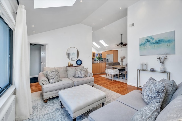 living area featuring radiator, visible vents, light wood finished floors, high vaulted ceiling, and a skylight