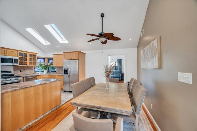 dining area featuring light wood-type flooring, visible vents, a ceiling fan, baseboards, and vaulted ceiling