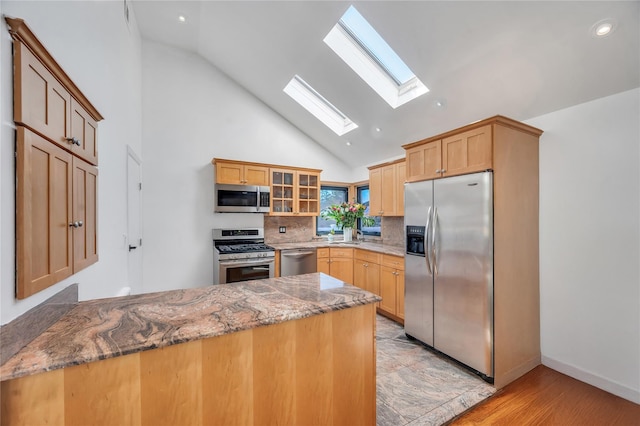 kitchen with glass insert cabinets, light stone countertops, decorative backsplash, a peninsula, and stainless steel appliances