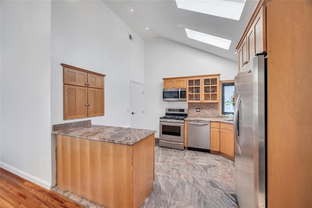 kitchen featuring glass insert cabinets, appliances with stainless steel finishes, a skylight, a peninsula, and stone countertops