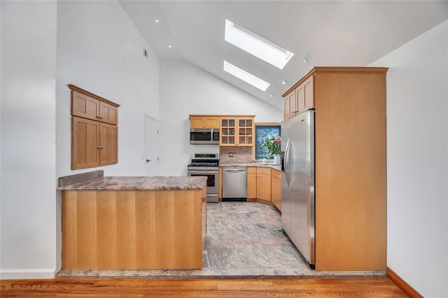 kitchen with decorative backsplash, appliances with stainless steel finishes, a skylight, a peninsula, and glass insert cabinets