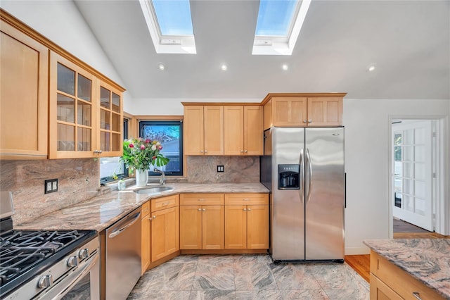 kitchen with light stone counters, lofted ceiling, a sink, glass insert cabinets, and appliances with stainless steel finishes