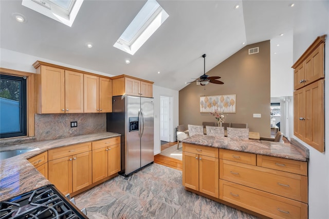 kitchen with visible vents, light stone countertops, a skylight, stainless steel refrigerator with ice dispenser, and a sink