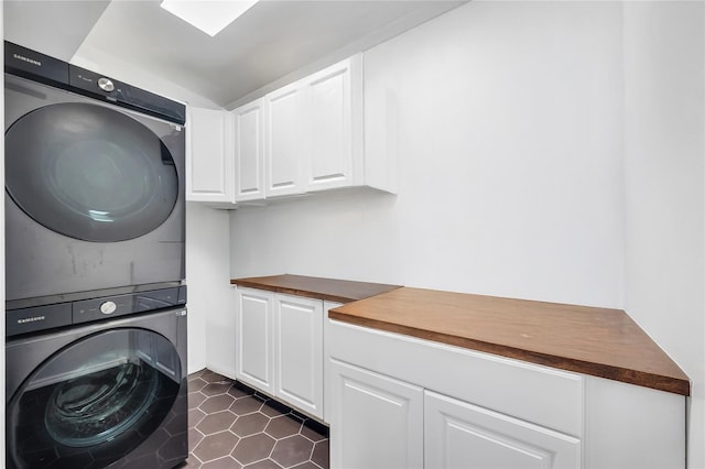 laundry area featuring cabinet space, stacked washer and dryer, and dark tile patterned flooring