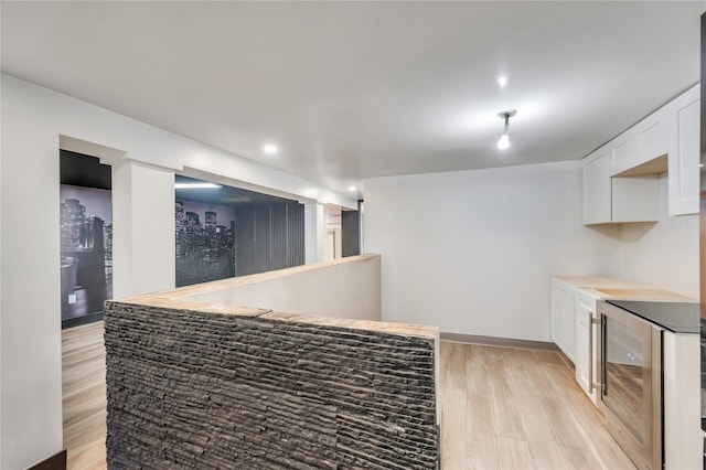 kitchen with light wood-type flooring, baseboards, beverage cooler, and white cabinetry