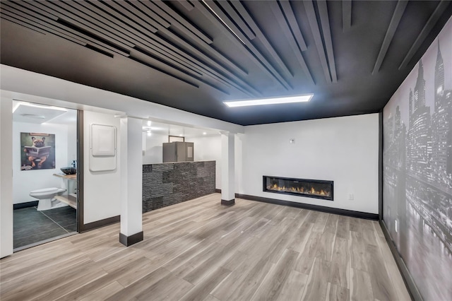 finished basement with a glass covered fireplace, light wood-style flooring, and baseboards