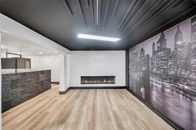 unfurnished living room featuring a glass covered fireplace, a city view, baseboards, and wood finished floors