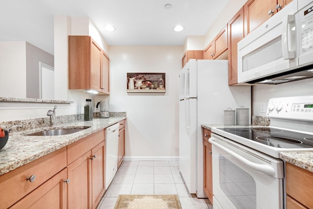 kitchen with a sink, light stone counters, white appliances, light tile patterned floors, and baseboards