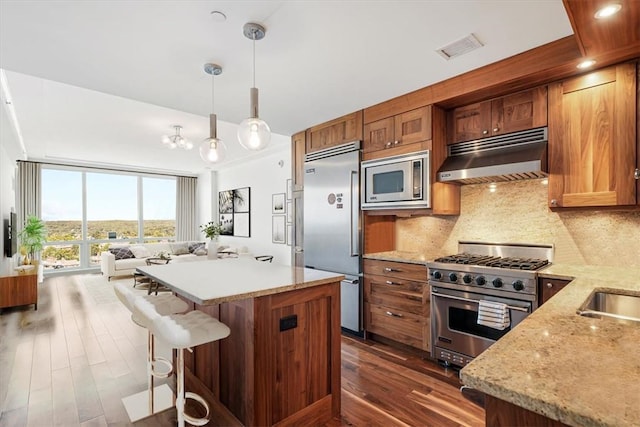 kitchen featuring visible vents, under cabinet range hood, built in appliances, decorative backsplash, and brown cabinets