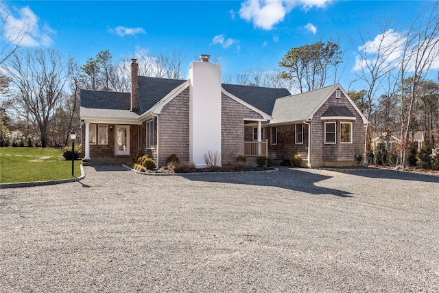 view of front facade featuring a front lawn, a chimney, driveway, and a shingled roof