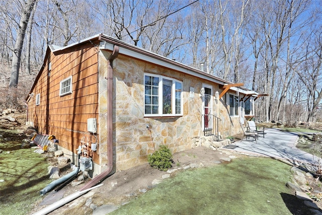 view of front facade with stone siding, a patio, and a front yard