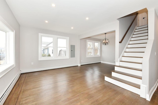 unfurnished living room featuring a baseboard heating unit, electric panel, wood finished floors, and stairs