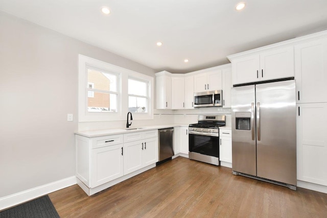 kitchen featuring light countertops, appliances with stainless steel finishes, wood finished floors, white cabinets, and a sink