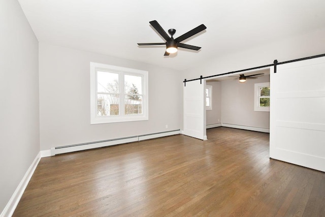 empty room featuring a ceiling fan, wood finished floors, baseboards, a baseboard radiator, and a barn door