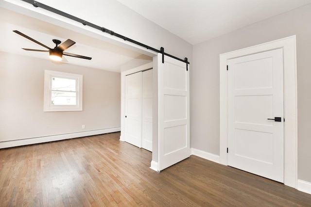 unfurnished bedroom featuring a baseboard heating unit, a barn door, wood finished floors, and baseboards