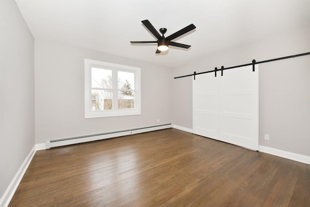 spare room featuring a baseboard heating unit, ceiling fan, baseboards, a barn door, and wood finished floors