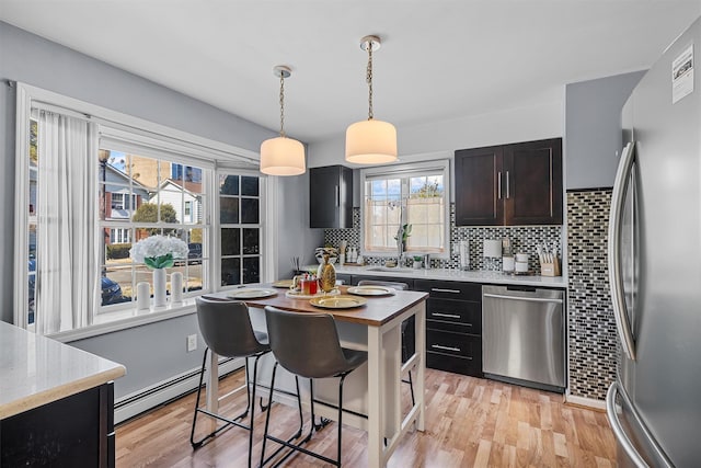 kitchen featuring baseboard heating, backsplash, appliances with stainless steel finishes, and light wood-style flooring