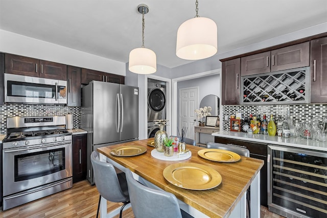 kitchen featuring stacked washer and dryer, beverage cooler, dark brown cabinetry, appliances with stainless steel finishes, and light countertops