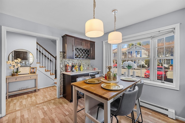 dining room featuring light wood finished floors, stairs, a baseboard heating unit, and a bar