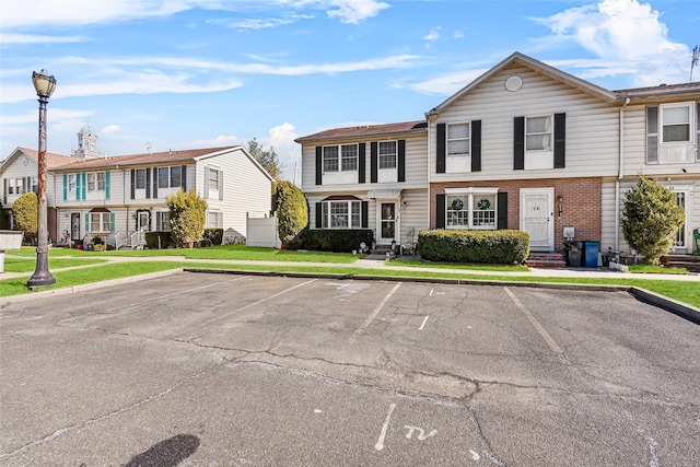 townhome / multi-family property with a front yard, uncovered parking, a residential view, entry steps, and brick siding