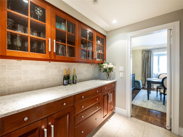 kitchen with light tile patterned floors, light stone countertops, baseboards, glass insert cabinets, and tasteful backsplash