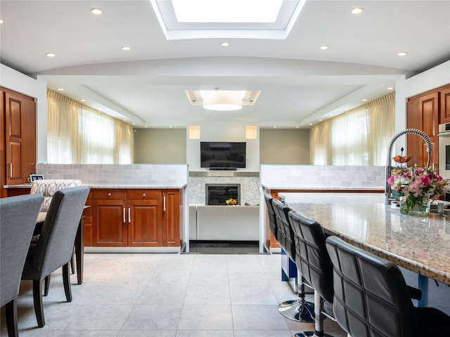 kitchen with light stone counters, decorative backsplash, a skylight, and a sink