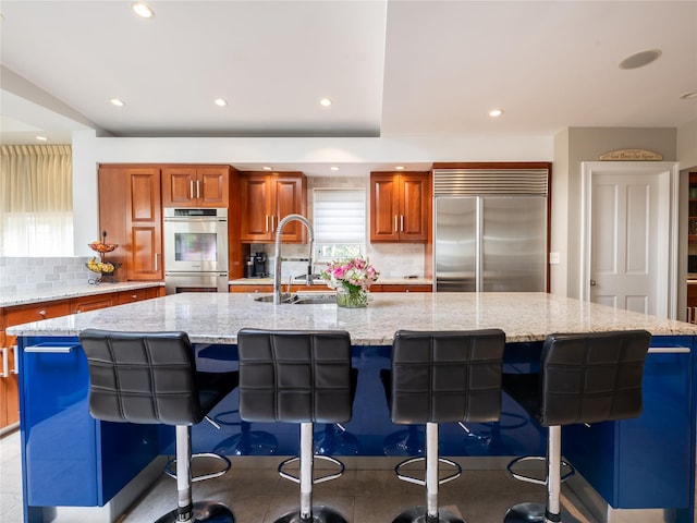 kitchen featuring brown cabinets, a sink, a spacious island, recessed lighting, and appliances with stainless steel finishes