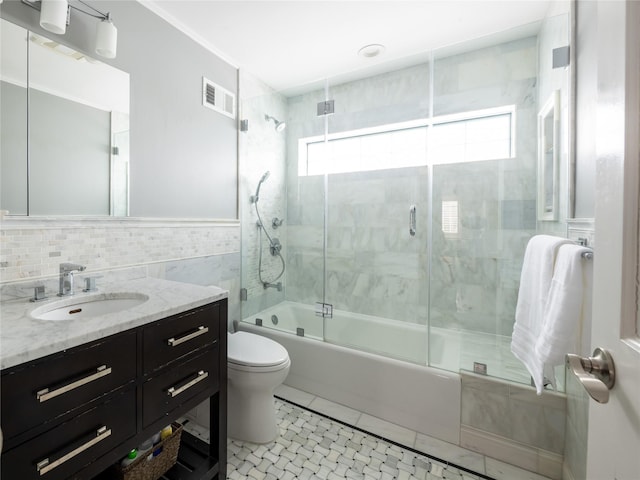 full bath featuring vanity, visible vents, bath / shower combo with glass door, tile walls, and toilet