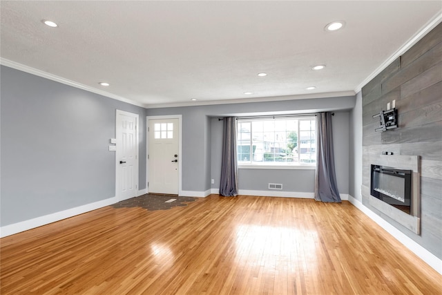 unfurnished living room with light wood-type flooring, a large fireplace, baseboards, and ornamental molding