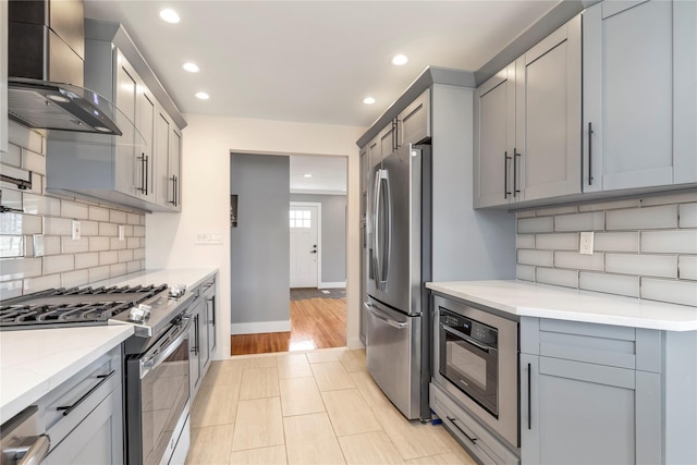 kitchen with tasteful backsplash, appliances with stainless steel finishes, gray cabinetry, and wall chimney range hood