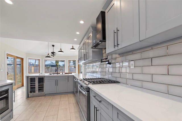 kitchen with beverage cooler, gray cabinets, tasteful backsplash, wall chimney exhaust hood, and stainless steel gas range