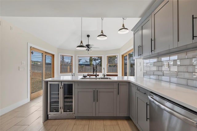 kitchen with beverage cooler, dishwasher, gray cabinets, a peninsula, and a sink